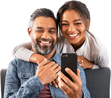 Seated man with woman's arm wrapped around shoulders looking at mobile device.