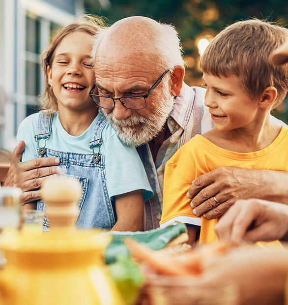man hugging grandchildren at outdoor dinner table