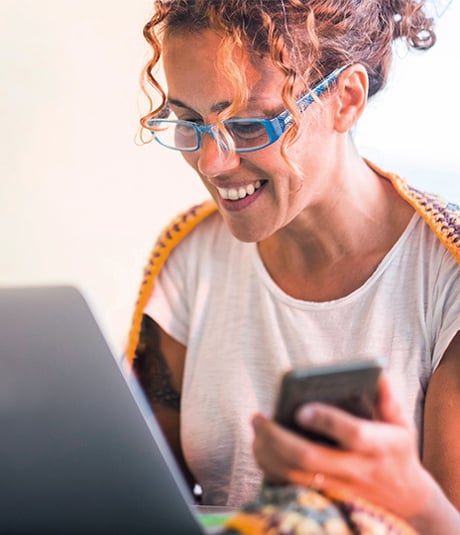 Woman holding phone and using laptop