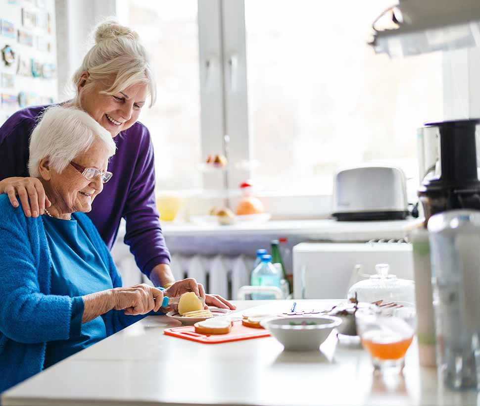 Elderly woman cutting fruit with woman looking over her shoulder